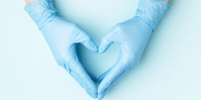 Hand in medical gloves. Doctor's hands in medical gloves in shape of heart on blue background. Banner for website with copy space.