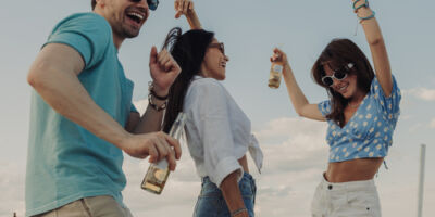 Happy young people enjoying cold beer while dancing on the beach together
